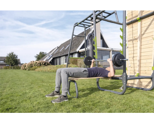 Mann trainiert mit einer Hantel auf einer Outdoor-Fitnessanlage im Garten.