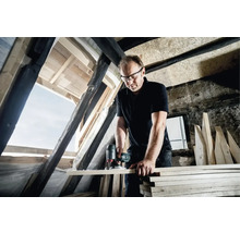 Ein Mann arbeitet mit einer Oberfräse an einem Holzbrett in einem Dachgeschoss.