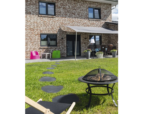 Außenbereich mit Feuerstelle, Liegestuhl, Wegplatten und Beschattung vor einem Wohnhaus