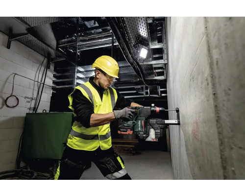 Ein Mann bohrt mit einem Bohrhammer ein Loch in eine Betonwand auf einer Baustelle.