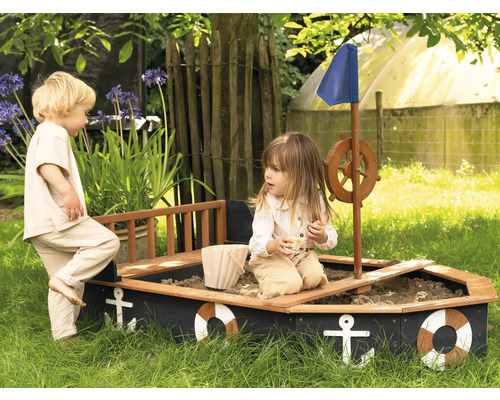 Zwei Kinder spielen in einem Sandkasten in Form eines Bootes im Garten.