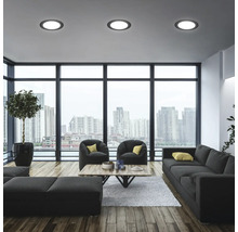 Modernes Wohnzimmer mit Sofa, Sesseln, Tisch und Deckenleuchten vor Fensterfront mit Stadtblick