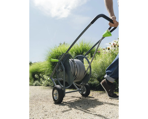 Person zieht einen Schlauchwagen mit Gartenschlauch im Garten.