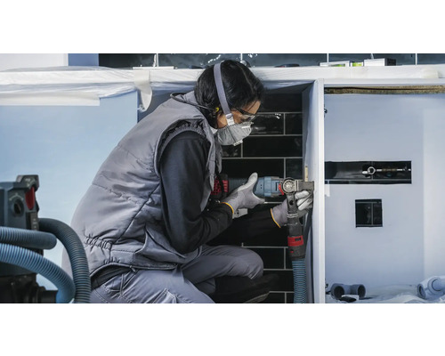 Eine Handwerkerin arbeitet mit einem Multifunktionswerkzeug an einem Badezimmerschrank.