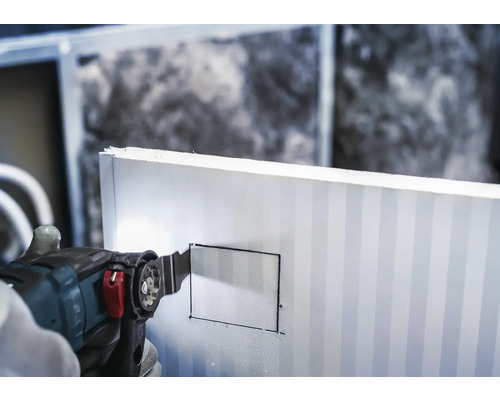 Eine Hand schneidet mit einem Multifunktionswerkzeug ein Rechteck in eine Dämmplatte.