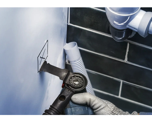 Oszillierendes Multifunktionswerkzeug beim Schneiden eines Lochs in eine Wand im Badezimmer.