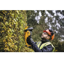 Ein Mann mit Schutzhelm und Schutzbrille schneidet eine Hecke mit einer Akku-Heckenschere von DeWalt.