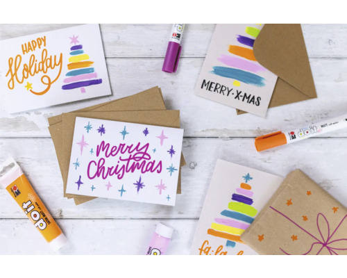 Weihnachtskarten mit weihnachtlichen Motiven und Farben, umgeben von Bastelmaterialien wie Stiften und Farben