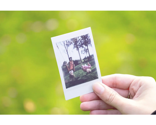 Hand hält Sofortbild mit Kindern auf Schaukeln