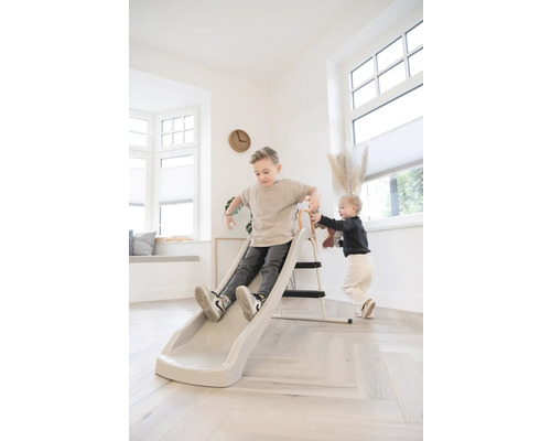 Zwei Kinder spielen im hellen Wohnzimmer mit einer Kinderrutsche mit Leiter.