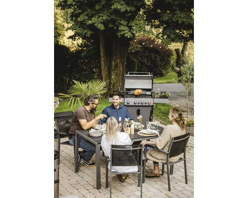 Szene im Freien mit einem Gasgrill, einem Esstisch und vier Personen beim Essen.