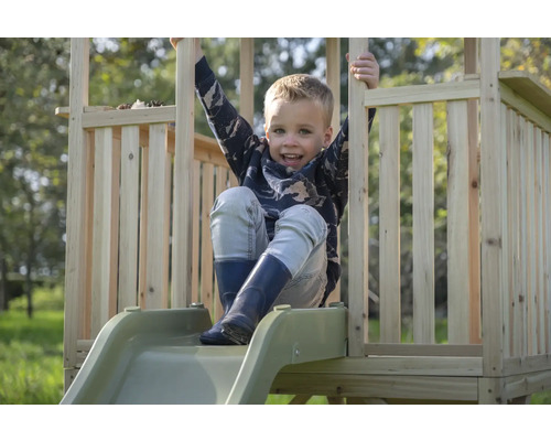 Ein Kind sitzt auf einer Holzrutsche mit Geländer auf einem Spielplatz