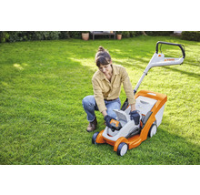 Eine Frau setzt eine Batterie in einen Rasenmäher von Stihl im Garten ein.