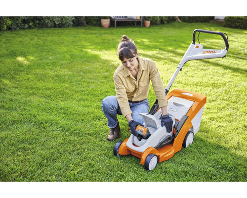 Eine Frau setzt eine Batterie in einen Rasenmäher von Stihl im Garten ein.