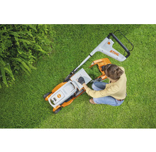 Frau bereitet Rasenmäher auf Rasen vor. Stihl Logo.