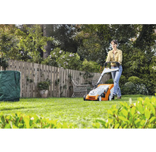 Frau bedient Rasenmäher im Garten mit Zaun, Rasenschnitt und Gartensack
