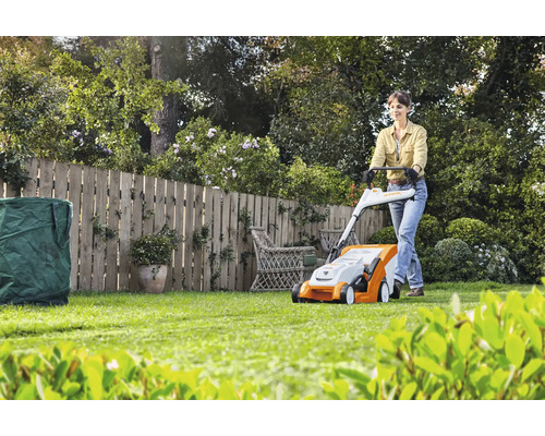 Frau bedient Rasenmäher im Garten mit Zaun, Rasenschnitt und Gartensack