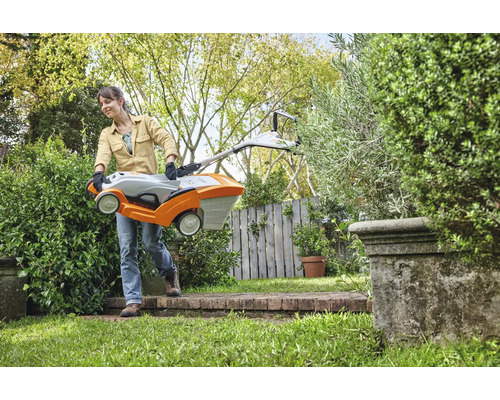 Eine Frau trägt einen Rasenmäher durch einen Garten.