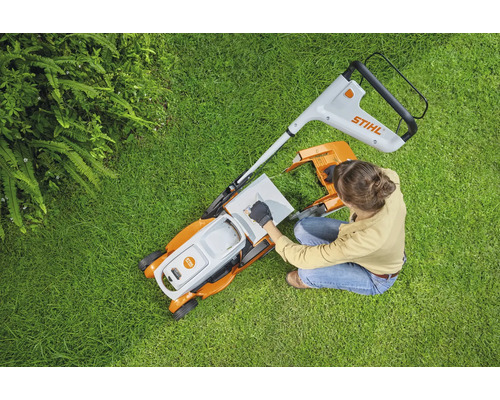 Aufsicht einer Frau, die einen Rasenmäher auf einer Rasenfläche vorbereitet. Stihl Logo.