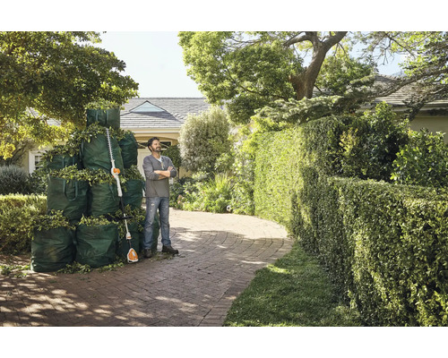 Mann steht neben Heckenschere und vollen Gartensäcken vor einem Haus.