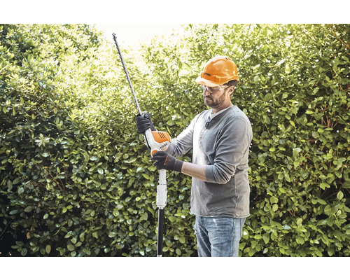 Mann mit Schutzhelm und Schutzbrille schneidet Hecke mit einer Heckenschere.