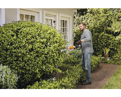 Ein Mann schneidet mit einer Heckenschere eine Hecke in einem Garten.