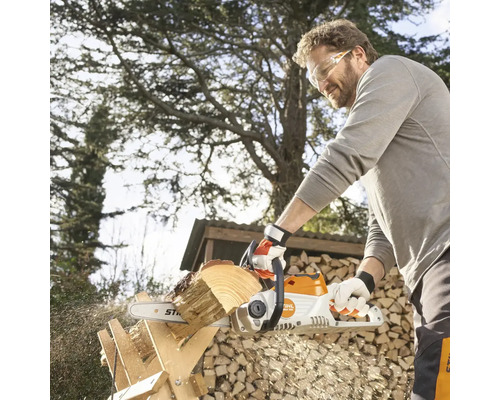 Mann sägt Holz mit einer Akku-Kettensäge von Stihl im Garten.