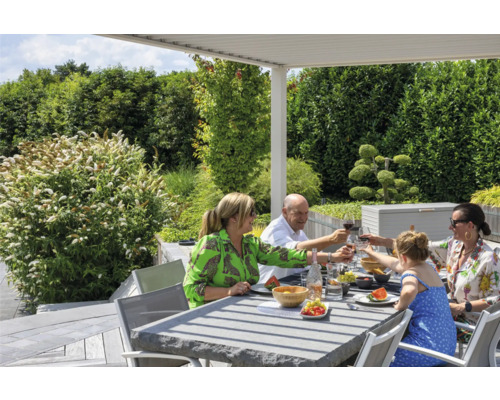Familie genießt Mahlzeit am Gartentisch unter einer Pergola im Freien