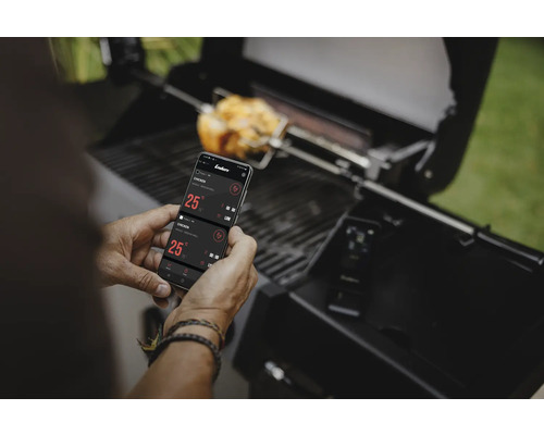 Mann bedient Grill mit Smartphone-App während Hähnchen grillt