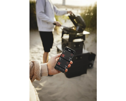 Eine Person grillt mit einem Grill und kontrolliert die Temperatur mit einer App auf einem Smartphone.
