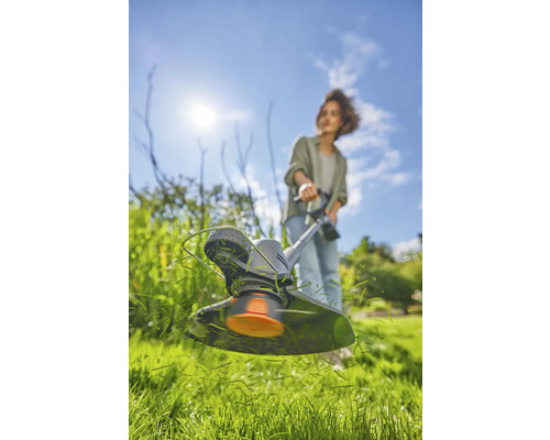Frau arbeitet mit einem Rasentrimmer im Garten.