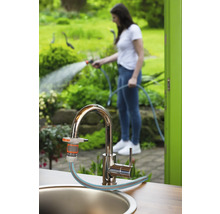 Gartenszene mit Wasserhahn, Gartenschlauchanschluss und Frau, die mit einem Gartenschlauch gießt