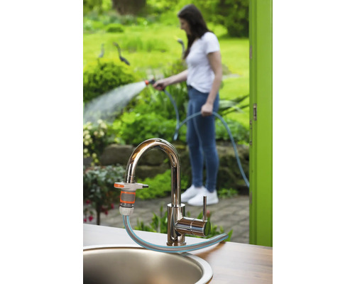 Gartenszene mit Wasserhahn, Gartenschlauchanschluss und Frau, die mit einem Gartenschlauch gießt