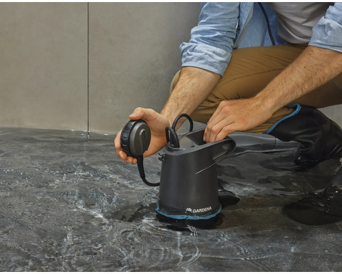 Ein Mann hockt auf dem Boden und bedient eine Gardena Schmutzwasserpumpe im Wasser.