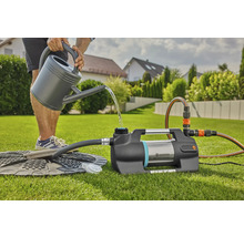 Eine Person gießt Wasser aus einer Gießkanne in eine Gardena Gartenpumpe auf einer Rasenfläche.