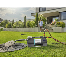 Gartenbewässerungsszene mit Pumpe, Schlauch und Regner vor einem Wohnhaus