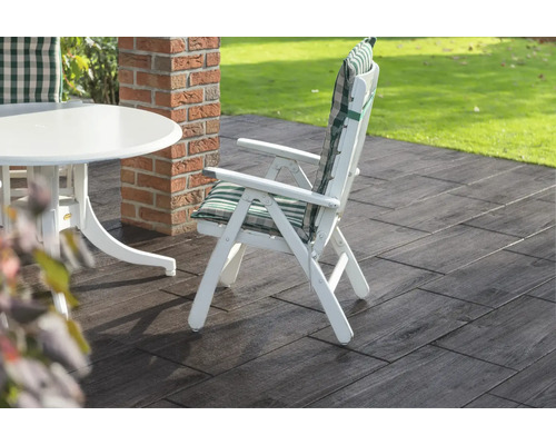 Gartenszene mit weißem Gartentisch, Gartenstuhl mit Polster und Bodenplatten