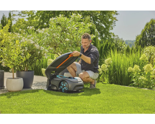 Mann öffnet den Deckel eines Rasenmähroboters auf einem Rasen