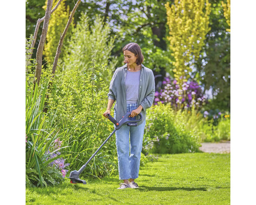 Frau schneidet Gras mit einem Rasentrimmer in einem Garten.