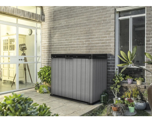 Gartengeräteschrank aus Kunststoff auf einer Terrasse vor einer Backsteinmauer.