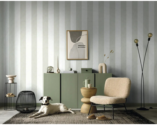 Wohnzimmer mit gestreifter Tapete, Kommode, Sessel, Stehlampe und Hund