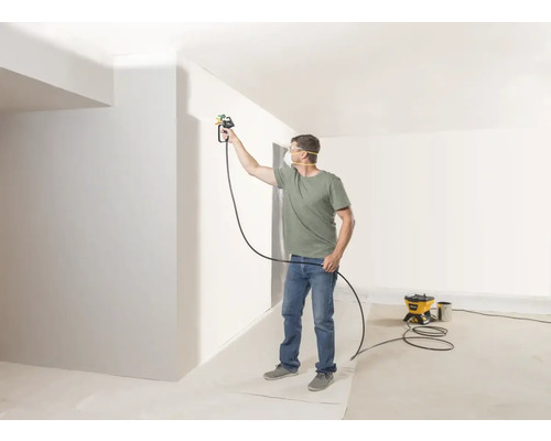 Mann streicht Wand mit Farbsprühsystem in hellem Raum