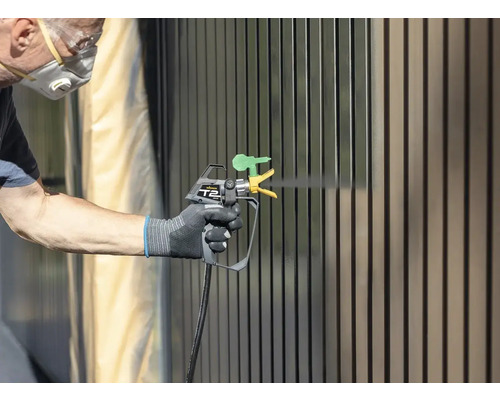 Person lackiert Zaun mit Farbsprühgerät