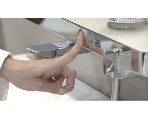 Eine Hand drückt einen Knopf an einer Armatur im Badezimmer.