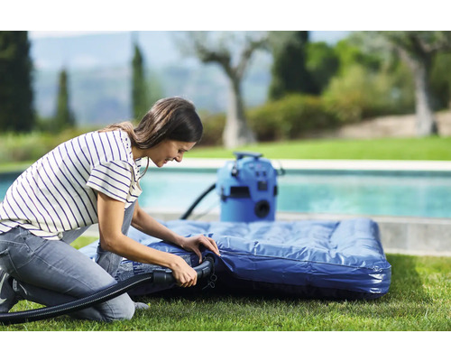 Frau pumpt Luftmatratze mit einer elektrischen Luftpumpe im Garten auf.