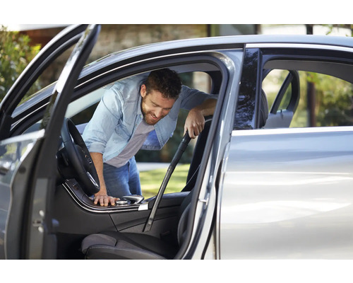 Ein Mann reinigt den Innenraum eines Autos mit einem Staubsauger.