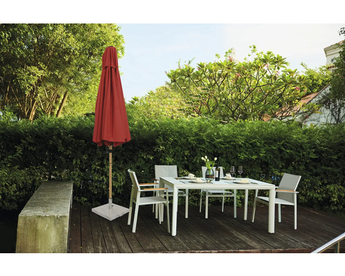 Gartenszene mit geschlossenem Sonnenschirm, Gartentisch und Gartenstühlen auf einer Holzterrasse vor einer grünen Hecke