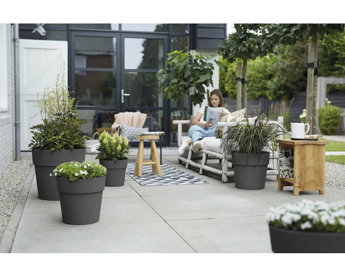Terrasse mit grauen Pflanzgefäßen und einer Frau, die auf einer Bank ein Buch liest