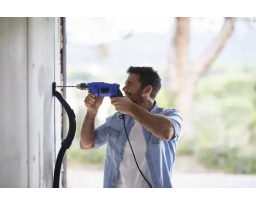 Ein Mann bohrt mit einer Bohrmaschine ein Loch in eine Wand für ein Elektrokabel.