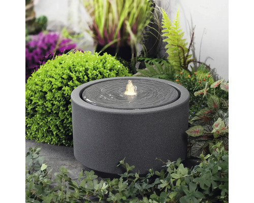 Runder Zimmerbrunnen aus Steinzeug mit Wasserspiel im Garten.